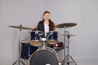 Açık gri arka planda bagetleri ve davulları olan genç bir kız.