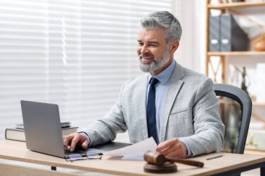 Ofiste dizüstü bilgisayar ve belgelerle çalışan gülümseyen noter.
