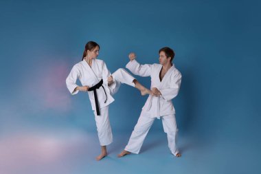 Üniformalı bir adam ve kadın açık mavi arka planda dumanlı karate yapıyorlar.