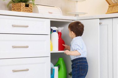 Evde çocuk güvenliği. Küçük çocuk mutfakta temizlik ürünleriyle dolap açıyor.