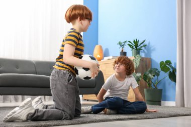 İki kardeş evde futbol topuyla oynuyor.