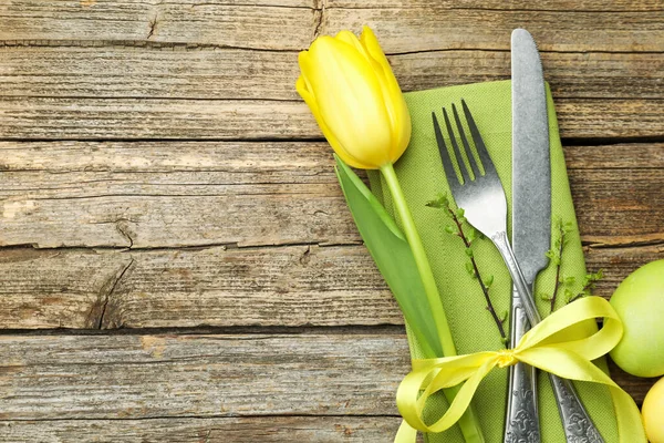 Easter table setting. Beautiful silverware with tulip and painted eggs on wooden background, top view. Space for text