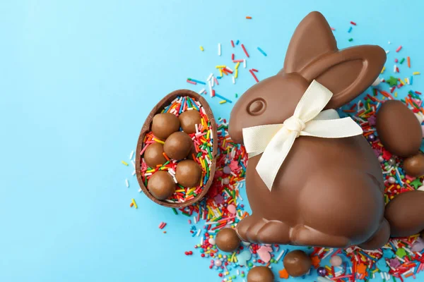 Çikolatalı Paskalya tavşanı, şekerli yumurta ve açık mavi arka planda serpiştirilmiş çikolata, düz yatak. Metin için boşluk