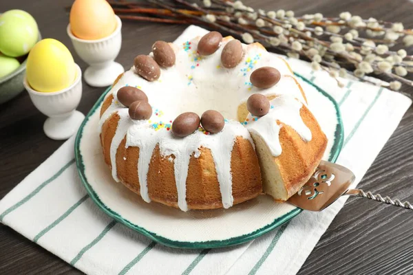 Lezzetli Paskalya pastası, boyalı yumurtalar, sunucu ve söğüt dalları ahşap masada, yakın plan.