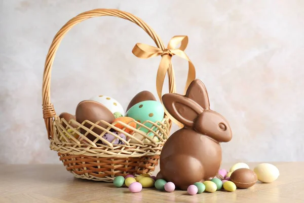 Çikolatalı Paskalya tavşanı ve hasır sepetteki yumurtalar ahşap masada açık gri arka planda, yakın plan