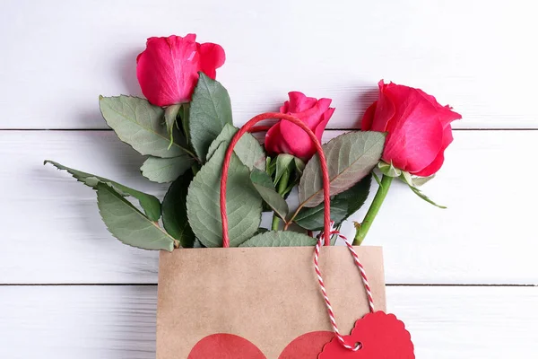 Beyaz ahşap arka planda güller olan hediye çantası, üst manzara. Sevgililer Günü