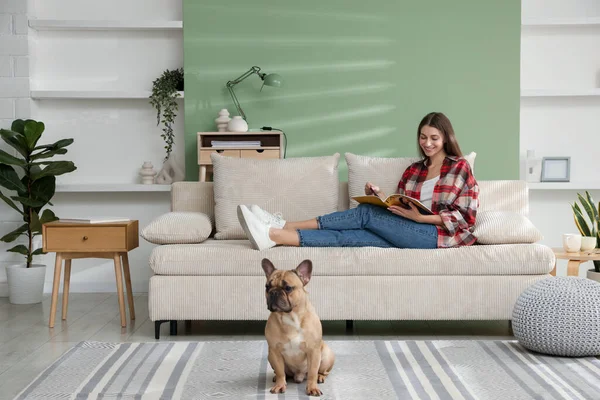 Dergisi olan bir kadın evdeki sevimli köpeğinin yanındaki kanepede dinleniyor.