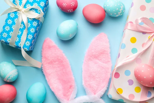 Mutlu Paskalyalar. Şirin tavşan kulakları, hediye kutuları ve açık mavi arka planda boyanmış yumurtalar, düz yatış.