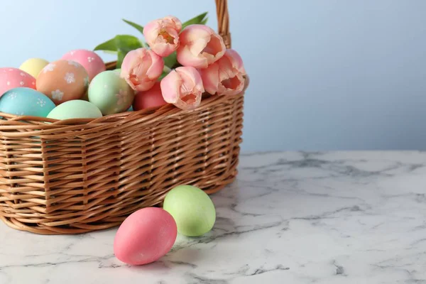 Boyanmış Paskalya yumurtaları ve hasır sepetteki güzel laleler beyaz mermer masa üzerinde, yakın plan. Metin için boşluk