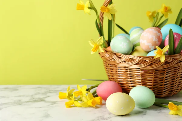Paskalya yumurtaları ve hasır sepetin içindeki güzel nergisler açık yeşil arka planda beyaz mermer masa üzerinde, yakın plan. Metin için boşluk