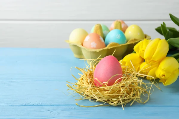 Kutuya boyanmış Paskalya yumurtaları, yuva ve açık mavi ahşap masa üzerinde güzel laleler, yakın plan. Metin için boşluk