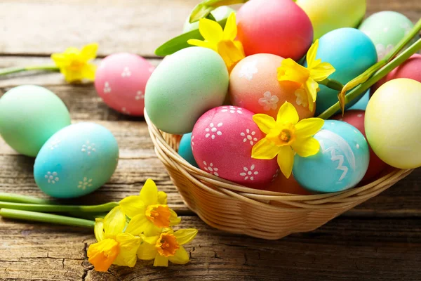Hasır sepete boyanmış Paskalya yumurtaları ve ahşap masaya güzel nergisler, yakın plan.