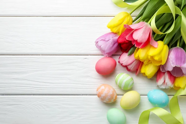 Boyalı Paskalya yumurtaları, güzel laleler ve beyaz ahşap masa şeritleri, düz bir döşeme. Metin için boşluk