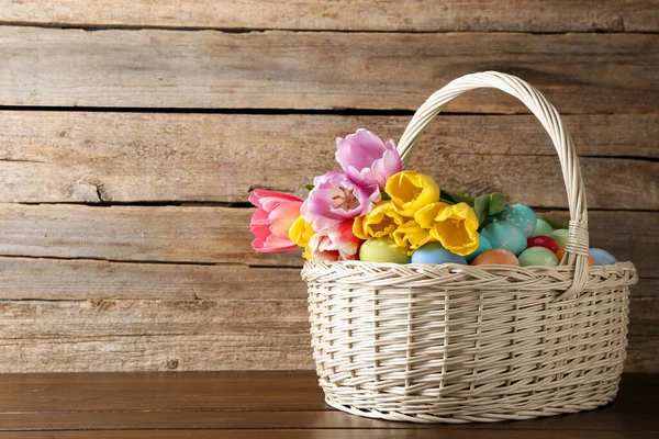 Hasır sepete boyanmış Paskalya yumurtaları ve ahşap masada güzel laleler. Metin için boşluk