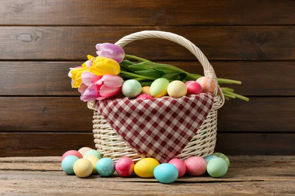 Hasır sepete boyanmış Paskalya yumurtaları ve ahşap masada güzel laleler.