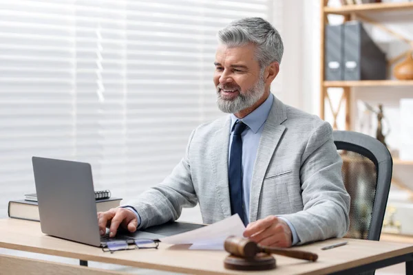 Ofiste dizüstü bilgisayar ve belgelerle çalışan gülümseyen noter.
