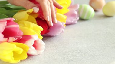 Güzel lalelere dokunan ve kutuya boyanmış Paskalya yumurtalarını gri desenli masaya koyan bir kadın.