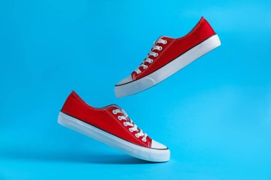 Açık mavi arka planda havada şık bir çift spor ayakkabı.