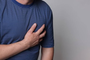 Kalp krizi geçirdi. Gri arka planda göğüs ağrısı çeken adam, yakın plan. Metin için boşluk