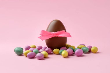 Yaylı çikolata yumurtası ve pembe arka planda renkli şekerler. Mutlu Paskalyalar