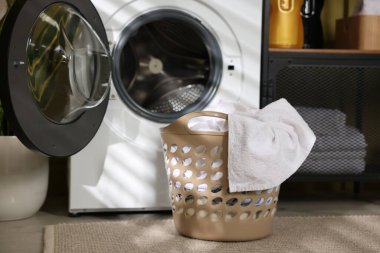 Çamaşır sepetinin içinde çamaşır makinesi ve deterjan var.