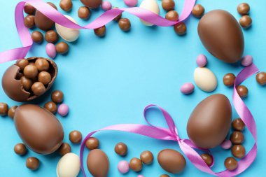 Çikolatalı Paskalya yumurtaları ve açık mavi arka planda menekşe kurdeleleri. Metin için boşluk