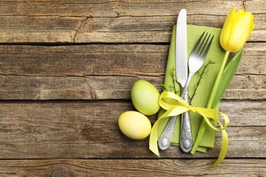 Easter table setting. Beautiful silverware with tulip and painted eggs on wooden background, top view. Space for text