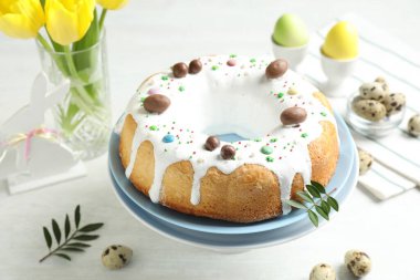 Delicious Easter cake, yellow tulips, quail and painted eggs on white table, closeup