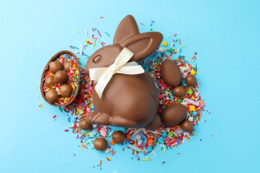 Çikolatalı Paskalya tavşanı, şekerli yumurta ve açık mavi arka planda serpiştirilmiş şeker, düz uzanmış