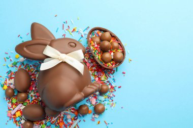 Çikolatalı Paskalya tavşanı, şekerli yumurta ve açık mavi arka planda serpiştirilmiş çikolata, düz yatak. Metin için boşluk