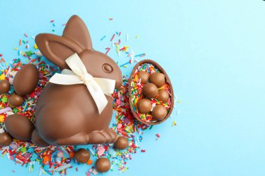 Çikolatalı Paskalya tavşanı, şekerli yumurta ve açık mavi arka planda serpiştirilmiş çikolata, düz yatak. Metin için boşluk