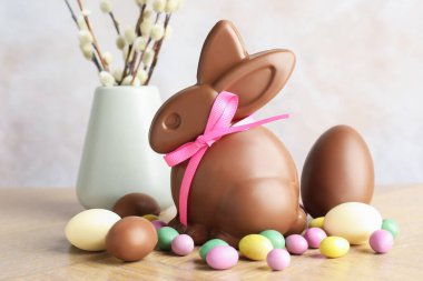 Çikolatalı Paskalya tavşanı, söğüt dalları ve yumurtalar açık gri arka planda, yakın plan.