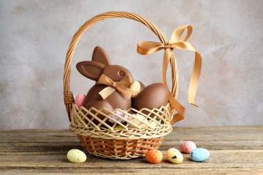 Çikolatalı Paskalya tavşanı ve hasır sepetteki yumurtalar ahşap masada açık gri arka planda, yakın plan