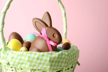 Çikolatalı Paskalya tavşanı ve hasır sepette pembe arka planda yumurtalar, yakın plan. Metin için boşluk