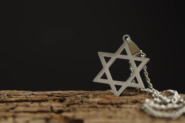 Soykırım Anma Günü. Davut Yıldızı şeklindeki kolye ve tahta yüzeyde siyah arka planda metal zincir, yakın plan. Metin için boşluk