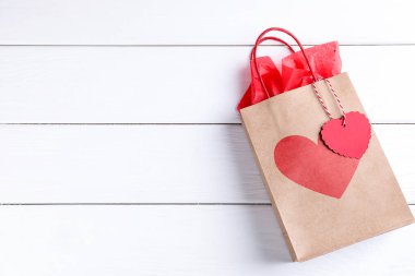 Beyaz ahşap arka planda kalbi olan hediye çantası, üst görünüm ve metin için yer. Sevgililer Günü