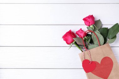 Beyaz ahşap arka planda güller, üst manzara ve metin için yer olan hediye çantası. Sevgililer Günü