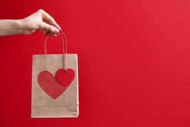 Kırmızı arka planda kalbi olan bir hediye çantası taşıyan kadın, yakın plan ve mesaj için yer. Sevgililer Günü
