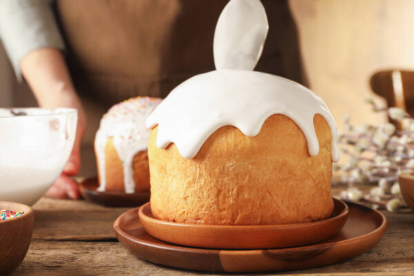 Woman putting glaze on Easter cake at wooden table, closeup