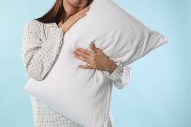 Açık mavi arka planda yastıklı şık pijamalı güzel kadın, yakın plan.