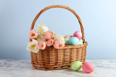 Boyanmış Paskalya yumurtaları ve sepetteki güzel laleler beyaz mermer masada.