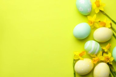 Painted Easter eggs and beautiful daffodils on light green background, flat lay. Space for text