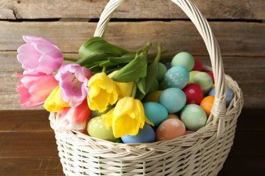 Hasır sepete boyanmış Paskalya yumurtaları ve ahşap masada güzel laleler, yakın plan.