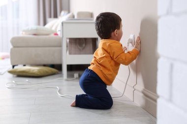 Evde çocuk güvenliği. Küçük çocuk içerideki elektrik prizinin fişini çekiyor, mesaj için yer var.