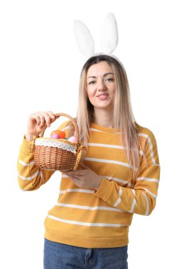 Paskalya kutlaması. Saç bandı takmış, tavşan kulaklı, hasırdan sepet dolusu beyaz arka planda boyalı yumurtaları olan gülümseyen bir kadın.