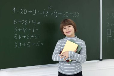 Matematik ödevi olan, karatahtanın yanında defterleri olan okul çocuğu.