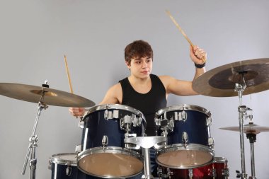 Çubuklu genç çocuk gri arka planda davul çalmayı öğreniyor.