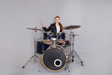 Açık gri arka planda bagetleri ve davulları olan genç bir kız.