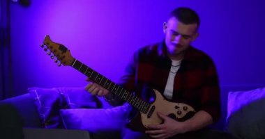 Elektro gitar çalan ve kapalı alanda renkli ışıklarla şarkı söyleyen bir adam. Kamera sağa hareket ediyor