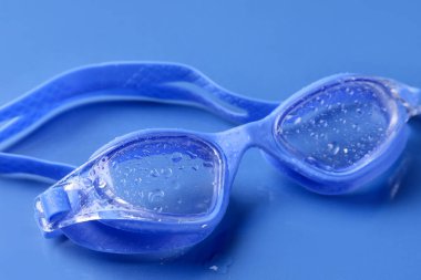 Mavi arka planda su damlaları olan yüzme gözlükleri, yakın plan